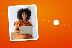 Smiling woman with curly hair sitting with a laptop on an orange background