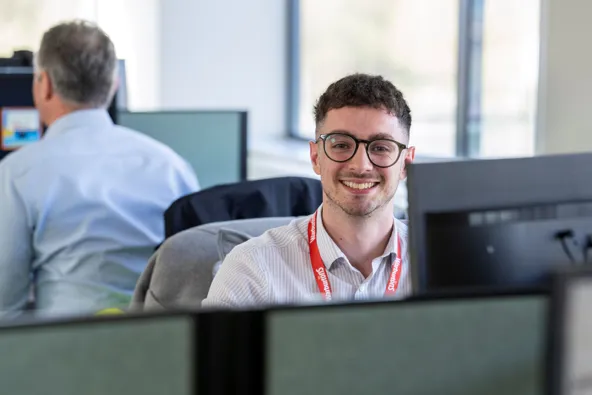 A smiling young man with glasses sitting at a desk in an office