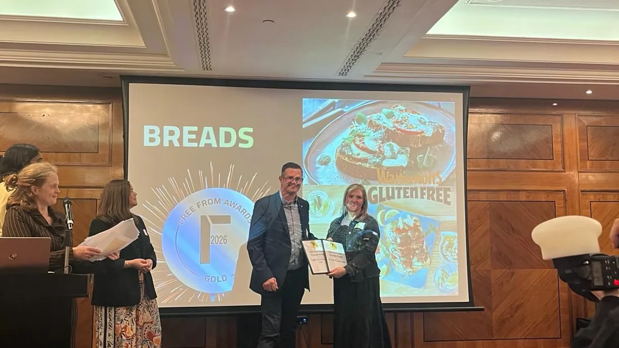 Award presentation at a ceremony featuring a man and a woman holding a certificate, with a screen displaying "Breads" and "Gluten Free
