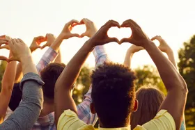 People forming heart shapes with their hands against a sunset backdrop