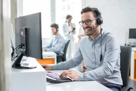 Man wearing headphones smiling while working at a computer in an office setting